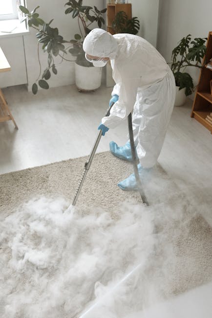 A person operating a yellow portable industrial fan or air mover during a surface cleaning or drying process, visible from the back with their hands on the equipment, positioned on a patterned carpet